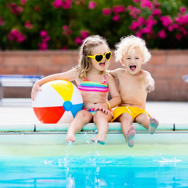2 children sitting on the side of a swimming pool with a beach ball